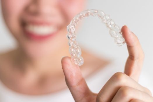 Close up of smiling person holding clear aligners in Edison