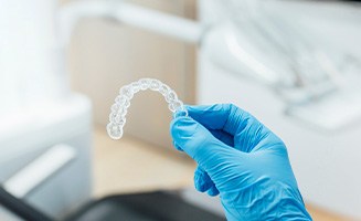 Dentist with blue glove holding clear aligner