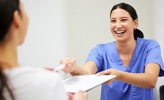 Smiling dental assistant handing patient forms