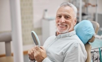 Smiling senior man holding mirror in dental chair