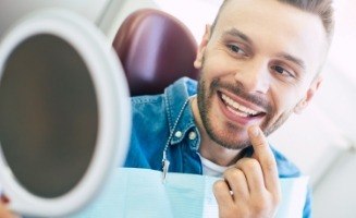 Dental patient pointing to his smile while looking in mirror