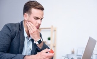 Businessman sitting at desk holding his cheek in pain