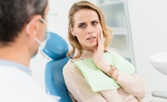 Woman holding cheek in pain while talking to emergency dentist