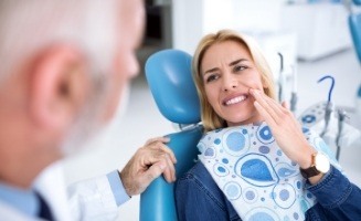 Woman holding side of her face in pain while talking to dentist