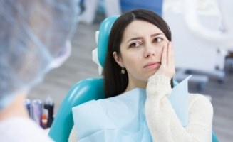 Woman holding side of her cheek in pain while talking to dentist