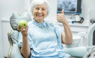 Woman holding an apple and giving a thumbs up from the patient’s chair