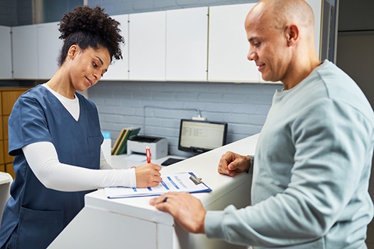 a front desk dental office staff member talking to a patient and filling out forms