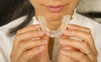 Close up of person holding Invisalign aligner in front of their mouth