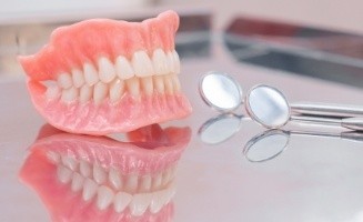 Full dentures resting on table with two dental mirrors