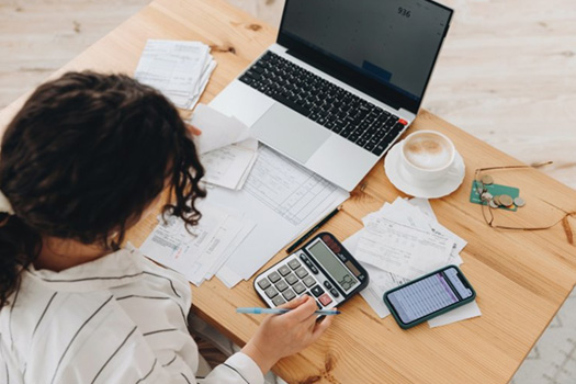 Woman using her laptop and a calculator at her desk