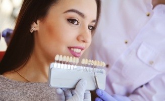Dentist holding row of veneers up to young woman's smile