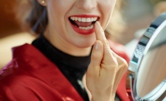 Close up of woman pointing to her smile while looking in mirror