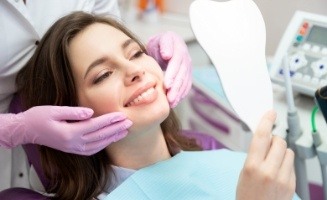 Young woman in dental chair admiring her smile in mirror