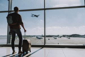 Man with suitcase at airport watching plane land