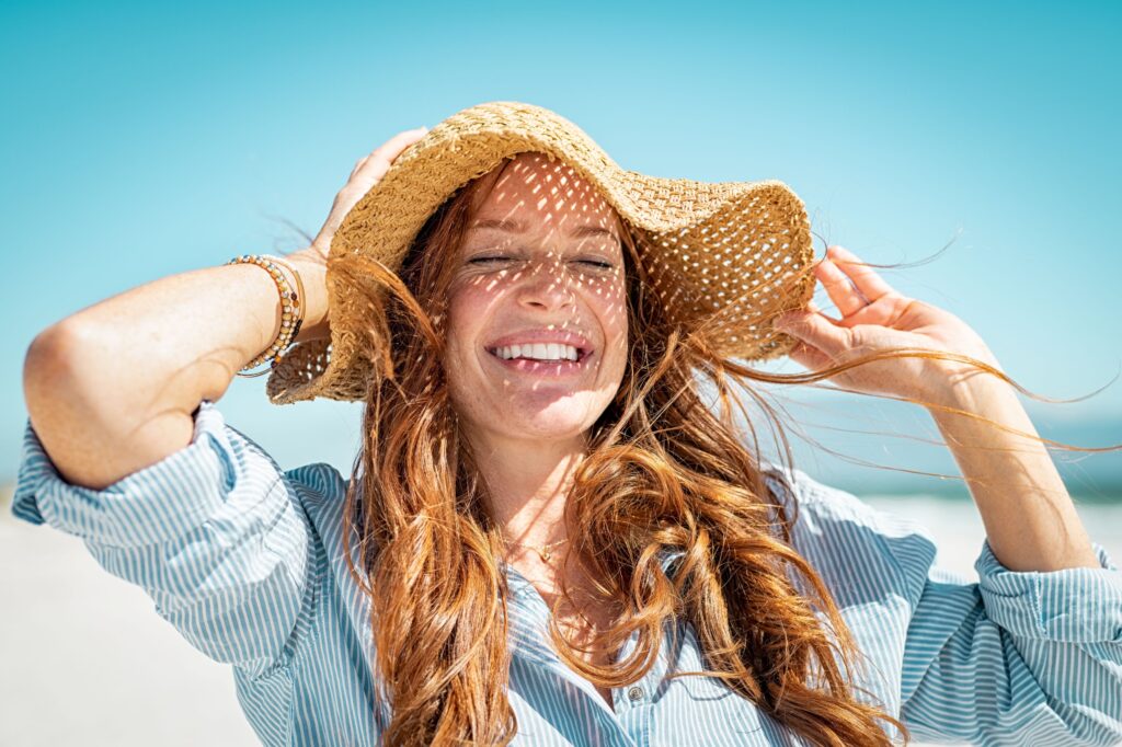 Woman with straw hat and eyes closed smiling at the beach